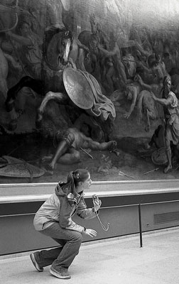 jeune fille qui se baisse devant un tableau de tr&egrave;s grande taille, comme pour &eacute;viter un obstacle. Le tableau rep&eacute;resente, entre autres, un cheval qui se cabre juste au-dessus d'elle. Photo en noir et blanc